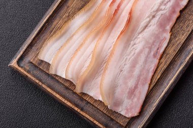 Baharat ve otlarla dilimlenmiş taze çiğ domuz pastırması ve koyu beton bir arka plan.