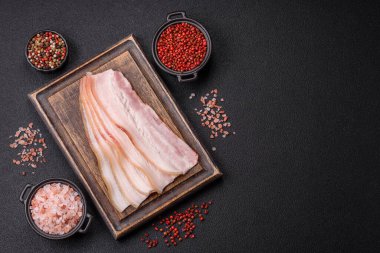 Baharat ve otlarla dilimlenmiş taze çiğ domuz pastırması ve koyu beton bir arka plan.