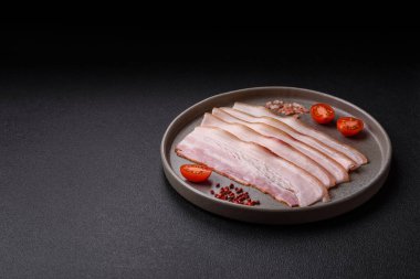 Baharat ve otlarla dilimlenmiş taze çiğ domuz pastırması ve koyu beton bir arka plan.