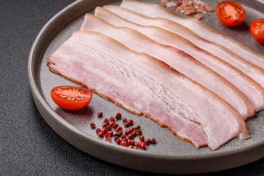 Baharat ve otlarla dilimlenmiş taze çiğ domuz pastırması ve koyu beton bir arka plan.
