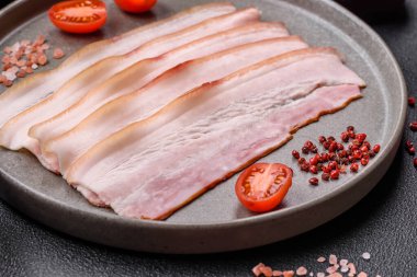 Baharat ve otlarla dilimlenmiş taze çiğ domuz pastırması ve koyu beton bir arka plan.