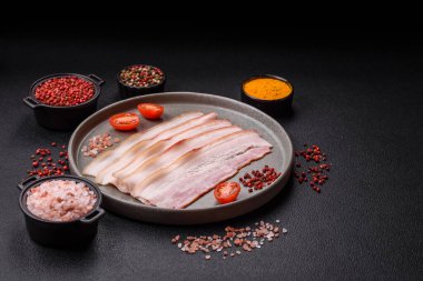 Baharat ve otlarla dilimlenmiş taze çiğ domuz pastırması ve koyu beton bir arka plan.