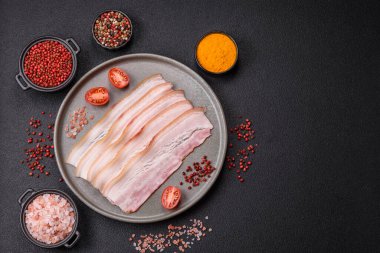 Baharat ve otlarla dilimlenmiş taze çiğ domuz pastırması ve koyu beton bir arka plan.