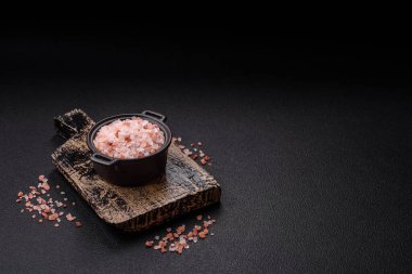 Koyu beton arka planda siyah bir kasede pembe Himalaya tuzu. Mutfakta baharatlar ve katkı maddeleri var.