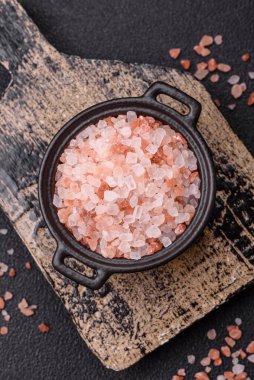 Koyu beton arka planda siyah bir kasede pembe Himalaya tuzu. Mutfakta baharatlar ve katkı maddeleri var.