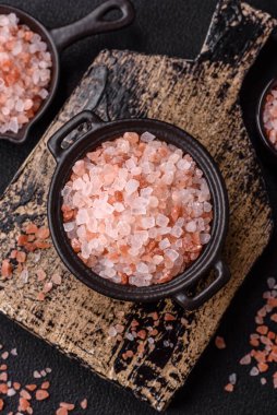 Koyu beton arka planda siyah bir kasede pembe Himalaya tuzu. Mutfakta baharatlar ve katkı maddeleri var.