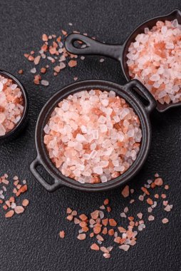 Koyu beton arka planda siyah bir kasede pembe Himalaya tuzu. Mutfakta baharatlar ve katkı maddeleri var.