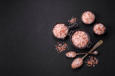 Koyu beton arka planda siyah bir kasede pembe Himalaya tuzu. Mutfakta baharatlar ve katkı maddeleri var.