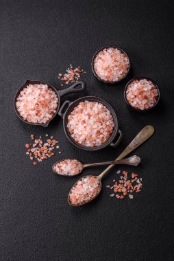 Koyu beton arka planda siyah bir kasede pembe Himalaya tuzu. Mutfakta baharatlar ve katkı maddeleri var.