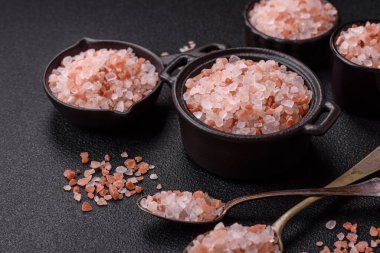 Koyu beton arka planda siyah bir kasede pembe Himalaya tuzu. Mutfakta baharatlar ve katkı maddeleri var.