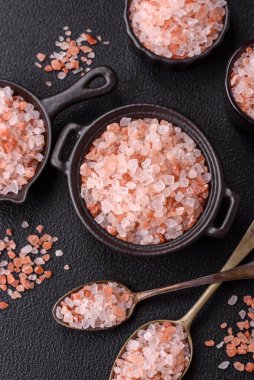 Koyu beton arka planda siyah bir kasede pembe Himalaya tuzu. Mutfakta baharatlar ve katkı maddeleri var.