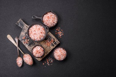 Koyu beton arka planda siyah bir kasede pembe Himalaya tuzu. Mutfakta baharatlar ve katkı maddeleri var.