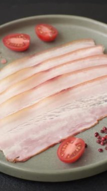 Baharat ve otlarla dilimlenmiş taze çiğ domuz pastırması ve koyu beton bir arka plan.