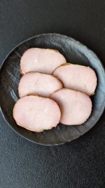 Et, tütsülenmiş, tuz, baharat ve otlarla dilimlenmiş koyu beton arka planda jambon.