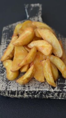 Koyu arkaplanda peynirli ve otlu fırında patates dilimleri. Ev yapımı organik sebze vejetaryen patates dilimleri.