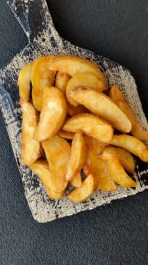 Koyu arkaplanda peynirli ve otlu fırında patates dilimleri. Ev yapımı organik sebze vejetaryen patates dilimleri.