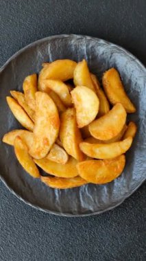 Koyu arkaplanda peynirli ve otlu fırında patates dilimleri. Ev yapımı organik sebze vejetaryen patates dilimleri.