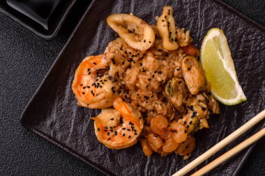 Karidesli pilav ve deniz ürünleri, sebze, baharat ve soya sosu koyu beton arka planda.