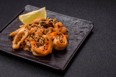 Karidesli pilav ve deniz ürünleri, sebze, baharat ve soya sosu koyu beton arka planda.