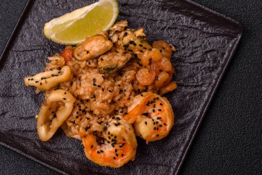 Karidesli pilav ve deniz ürünleri, sebze, baharat ve soya sosu koyu beton arka planda.