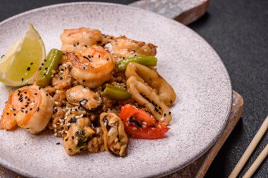 Karidesli pilav ve deniz ürünleri, sebze, baharat ve soya sosu koyu beton arka planda.