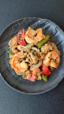 Karidesli pilav ve deniz ürünleri, sebze, baharat ve soya sosu koyu beton arka planda.