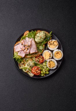 Kaynamış yumurta, jambon, domates, yeşil fasulye, koyu beton arkaplanda aioli sosu içeren sağlıklı bir kahvaltı.