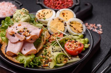 Kaynamış yumurta, jambon, domates, yeşil fasulye, koyu beton arkaplanda aioli sosu içeren sağlıklı bir kahvaltı.