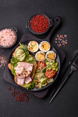 Kaynamış yumurta, jambon, domates, yeşil fasulye, koyu beton arkaplanda aioli sosu içeren sağlıklı bir kahvaltı.