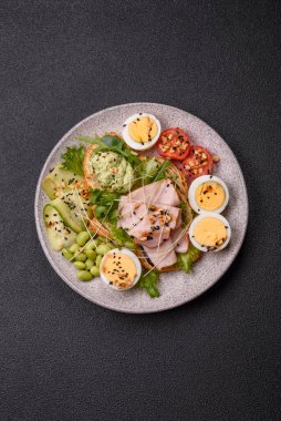 Kaynamış yumurta, jambon, domates, yeşil fasulye, koyu beton arkaplanda aioli sosu içeren sağlıklı bir kahvaltı.