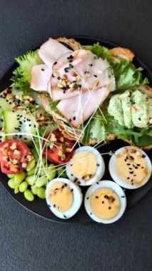 Kaynamış yumurta, jambon, domates, yeşil fasulye, koyu beton arkaplanda aioli sosu içeren sağlıklı bir kahvaltı.