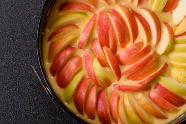 Koyu beton arka planda pişirmek için hazırlanmış kalıplı çiğ elmalı turta.