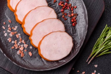 Lezzetli taze jambon, tuz, baharat ve otlarla kesilmiş koyu beton arka planda yuvarlak dilimler halinde.