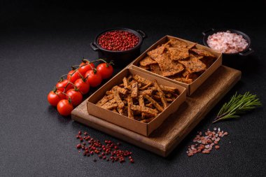 Koyu beton arka planda tohum ve tahıllı, tuzlu, baharatlı ve otlu ev yapımı kahverengi ekmek krakerleri veya kızarmış ekmekler.