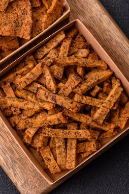 Koyu beton arka planda tohum ve tahıllı, tuzlu, baharatlı ve otlu ev yapımı kahverengi ekmek krakerleri veya kızarmış ekmekler.