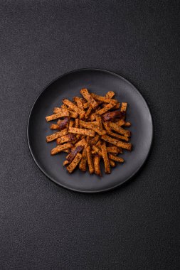 Koyu beton arka planda tohum ve tahıllı, tuzlu, baharatlı ve otlu ev yapımı kahverengi ekmek krakerleri veya kızarmış ekmekler.