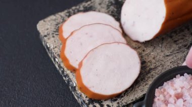 Lezzetli taze jambon, tuz, baharat ve otlarla kesilmiş koyu beton arka planda yuvarlak dilimler halinde.