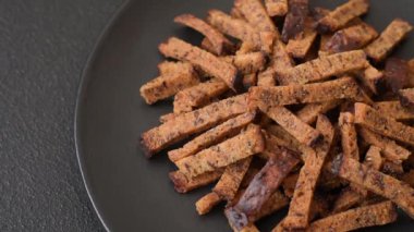 Koyu beton arka planda tohum ve tahıllı, tuzlu, baharatlı ve otlu ev yapımı kahverengi ekmek krakerleri veya kızarmış ekmekler.