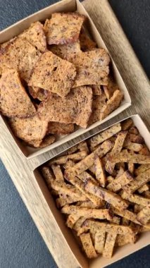 Koyu beton arka planda tohum ve tahıllı, tuzlu, baharatlı ve otlu ev yapımı kahverengi ekmek krakerleri veya kızarmış ekmekler.