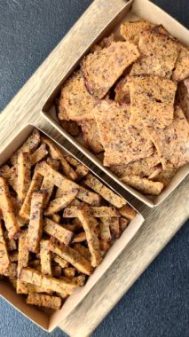 Koyu beton arka planda tohum ve tahıllı, tuzlu, baharatlı ve otlu ev yapımı kahverengi ekmek krakerleri veya kızarmış ekmekler.