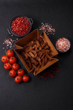 Koyu beton arka planda tohum ve tahıllı, tuzlu, baharatlı ve otlu ev yapımı kahverengi ekmek krakerleri veya kızarmış ekmekler.