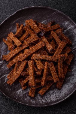 Koyu beton arka planda tohum ve tahıllı, tuzlu, baharatlı ve otlu ev yapımı kahverengi ekmek krakerleri veya kızarmış ekmekler.