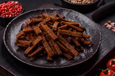 Koyu beton arka planda tohum ve tahıllı, tuzlu, baharatlı ve otlu ev yapımı kahverengi ekmek krakerleri veya kızarmış ekmekler.