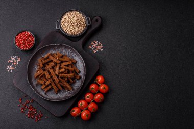 Koyu beton arka planda tohum ve tahıllı, tuzlu, baharatlı ve otlu ev yapımı kahverengi ekmek krakerleri veya kızarmış ekmekler.