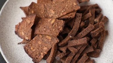 Koyu beton arka planda tohum ve tahıllı, tuzlu, baharatlı ve otlu ev yapımı kahverengi ekmek krakerleri veya kızarmış ekmekler.