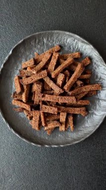 Koyu beton arka planda tohum ve tahıllı, tuzlu, baharatlı ve otlu ev yapımı kahverengi ekmek krakerleri veya kızarmış ekmekler.