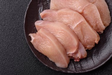 Çiğ tavuk ya da hindi filetosu. Tuz, baharat ve otlarla dilimlenmiş koyu beton arka planda.