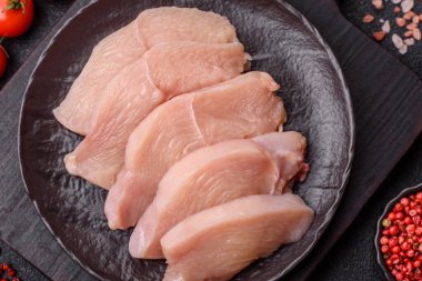 Çiğ tavuk ya da hindi filetosu. Tuz, baharat ve otlarla dilimlenmiş koyu beton arka planda.