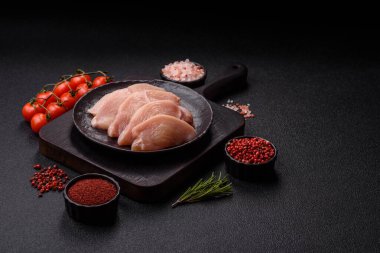 Çiğ tavuk ya da hindi filetosu. Tuz, baharat ve otlarla dilimlenmiş koyu beton arka planda.