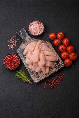 Çiğ tavuk ya da hindi filetosu. Tuz, baharat ve otlarla dilimlenmiş koyu beton arka planda.